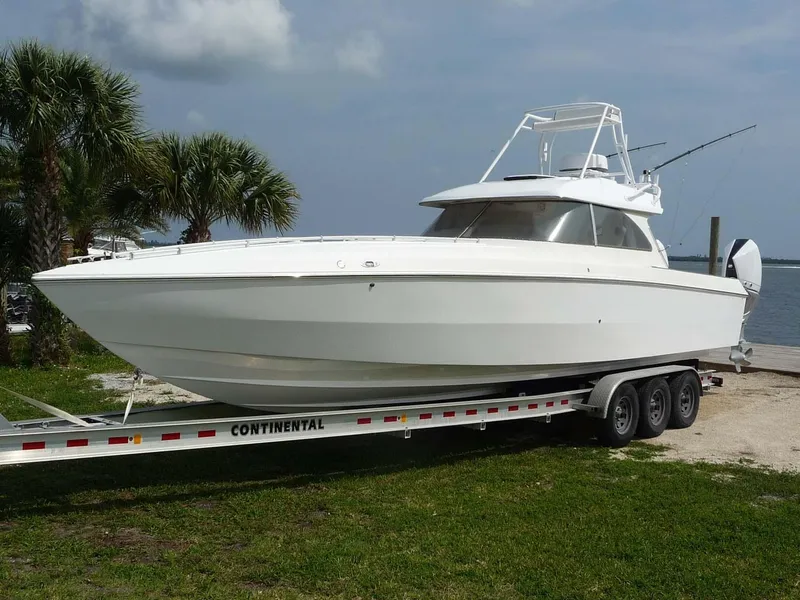 The Image of 1985 Wellcraft Scarab 34 boat on trailer, parked near palm trees and waterfront. - 0