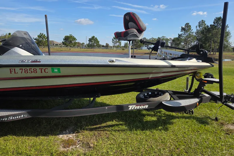 Slide: The Image of 2021 Triton 20 TrX boat on trailer, parked on grassy area near water. - 3