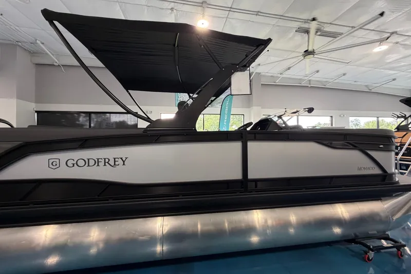 Slide: The Image of 2026 Godfrey Monaco 235ULC pontoon boat displayed indoors with sleek design and canopy. - 9
