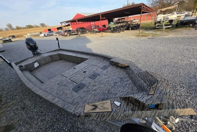 Slide: The Image of 2026 Xpress X18DB boat on trailer, camo design, parked on gravel lot. - 27