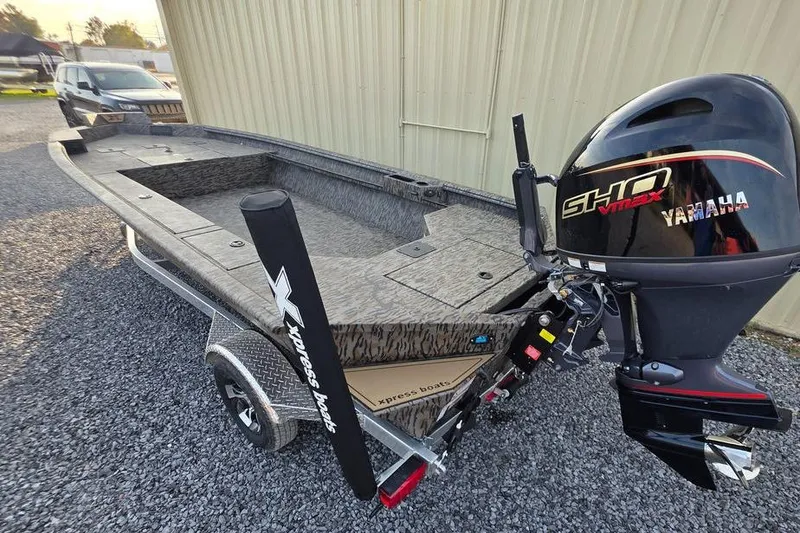Slide: The Image of 2026 Xpress X18DB boat rear view with motor on gravel surface. - 9