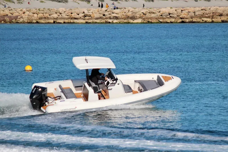 The Image of 2026 Northstar Orion 7 boat cruising on clear blue water near rocky shoreline. - 0