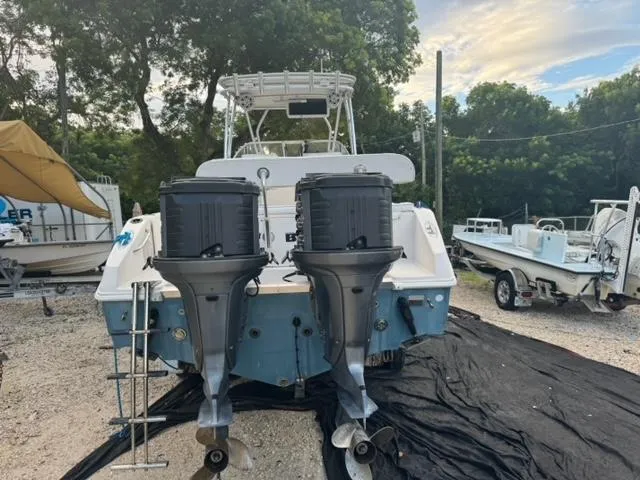 Slide: The Image of 2007 Cobia 270 boat with dual outboard motors, parked on gravel near trees and other boats. - 3