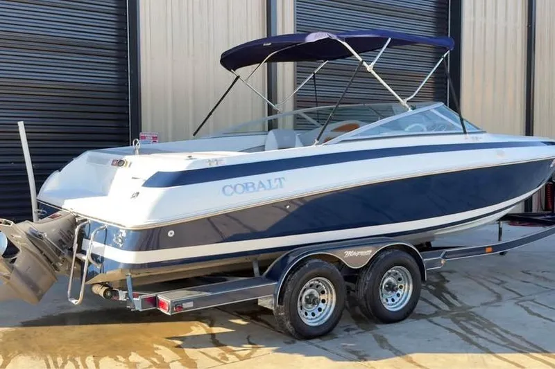 The Image of 1998 Cobalt 220 boat on trailer, blue and white design, parked near a building. - 1