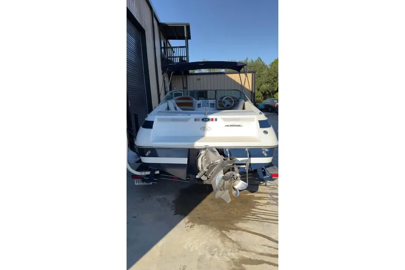 Slide: The Image of 1998 Cobalt 220 boat, rear view, parked near a building, showcasing propeller and interior. - 13