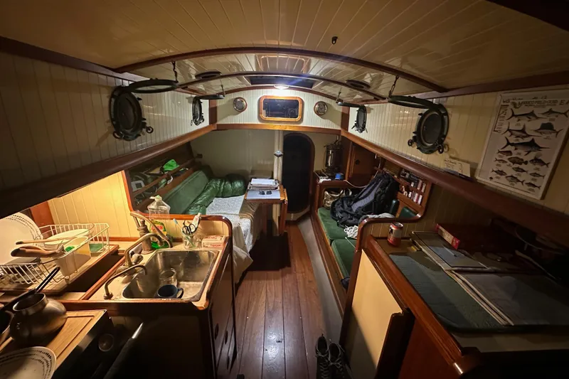 Slide: The Image of Cozy interior of a 2000 Sam L. Morse Bristol Channel Cutter 28 sailboat, featuring a compact kitchen and seating area. - 3