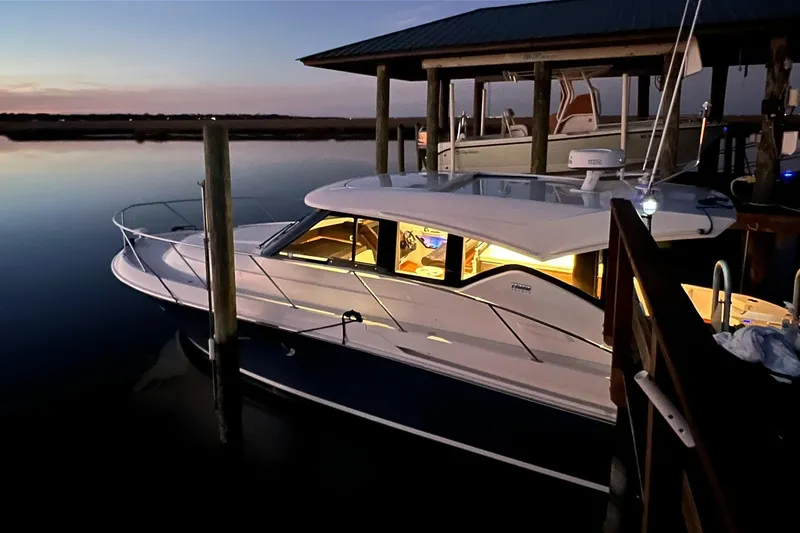Slide: The Image of 2017 Tiara Yachts C39 Coupe docked at sunset, illuminated interior, serene water setting. - 4