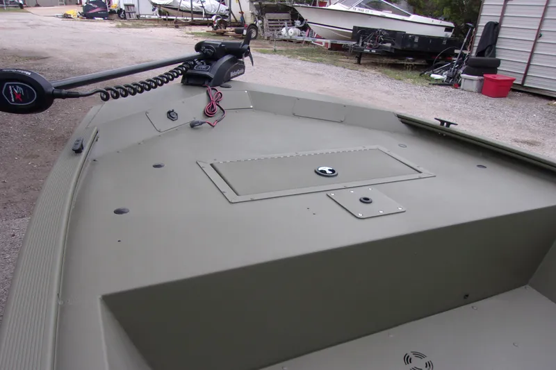 Slide: The Image of 2022 Tracker Grizzly 1648 MVX SC boat deck with trolling motor in a yard setting. - 9