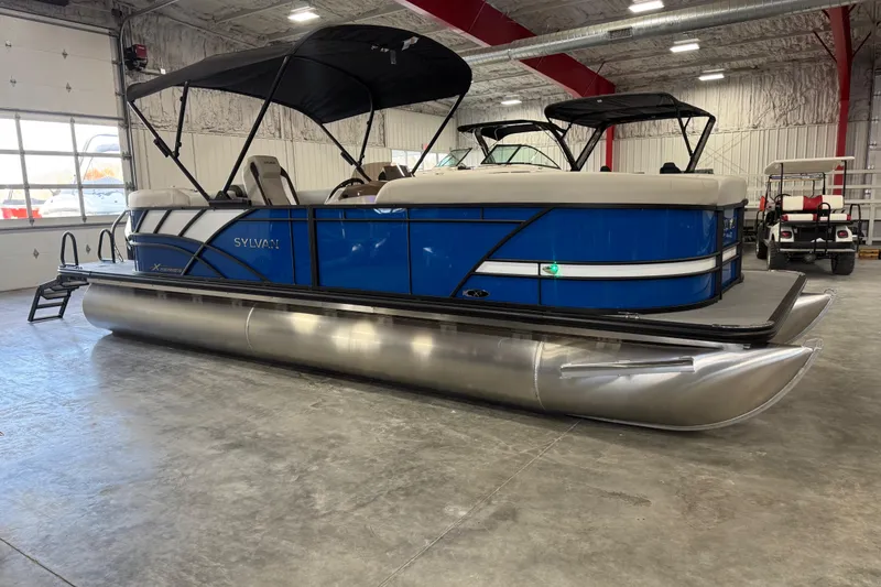 The Image of 2026 Sylvan X5 pontoon boat in showroom, featuring blue exterior and black canopy. - 1