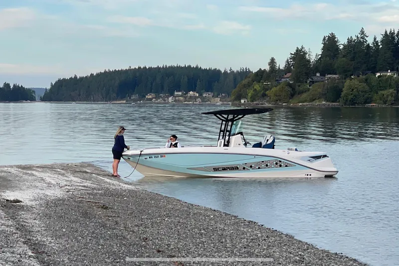 Slide: The Image of 2018 Scarab 255 Open ID boat near shore with two people, scenic forested background. - 6