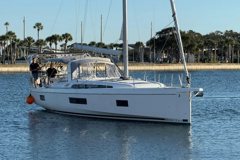 Slide: The Image of 2020 Beneteau Oceanis 51.1 sailboat on calm water near a palm-lined shore. - 2