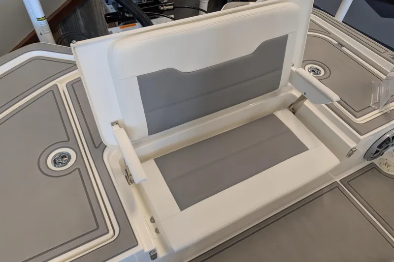 Slide: The Image of 2026 Mako 24 APEX boat seat with gray and white upholstery, open storage compartment. - 13