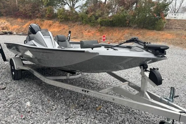 Slide: The Image of 2026 Xpress H18 Bass boat on trailer, parked on gravel with trees in background. - 12