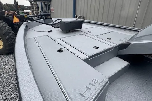 Slide: The Image of 2026 Xpress H18 Bass boat deck with storage compartments, parked on gravel. - 4