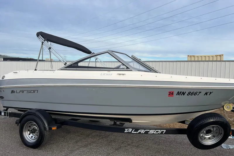 Slide: The Image of 2013 Larson LX 205S IO boat on trailer, gray and white exterior, parked outdoors. - 2