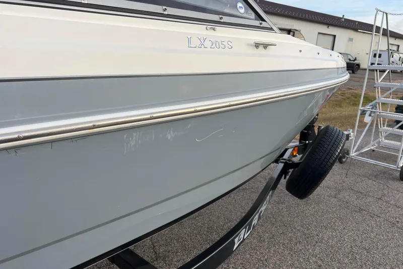 Slide: The Image of 2013 Larson LX 205S IO boat on trailer, parked near industrial buildings. - 44