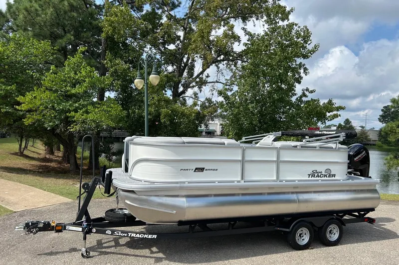 The Image of 2026 Sun Tracker Party Barge 20 Classic Series pontoon boat on trailer, parked near trees. - 1