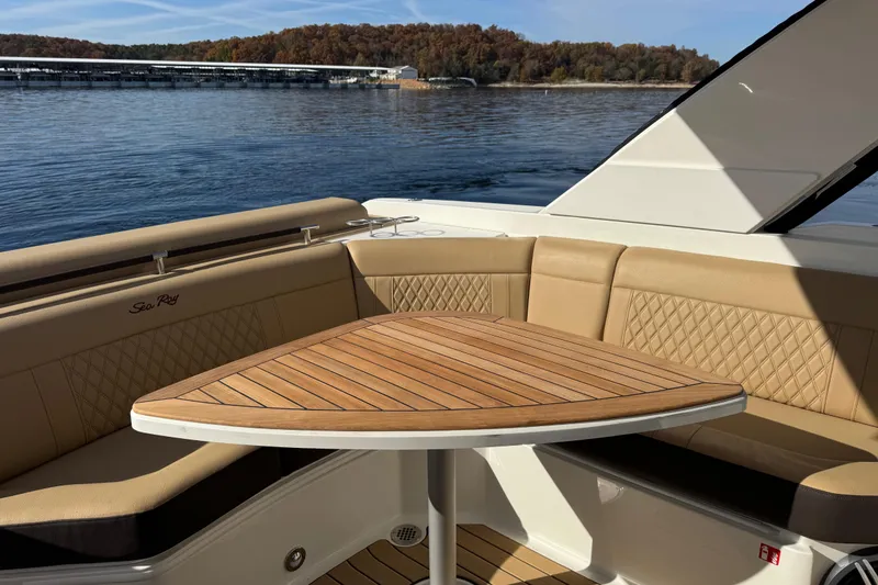 Slide: The Image of 2026 Sea Ray SLX 310 boat interior with tan seating and wooden table on a calm lake. - 11