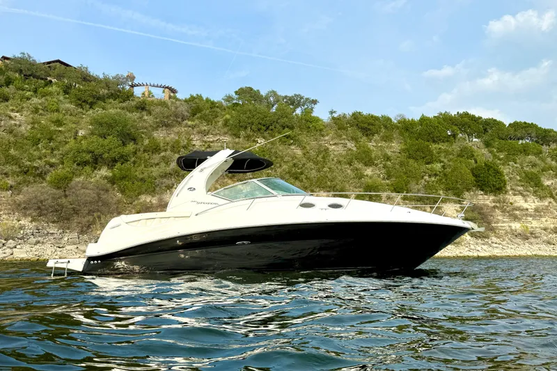The Image of 2006 Sea Ray 320 Sundancer boat on water, with lush green hillside background. - 1