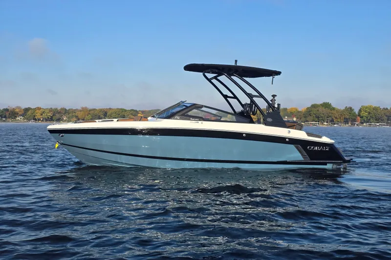 The Image of 2022 Cobalt R4 Surf boat on a calm lake under a clear blue sky. - 1