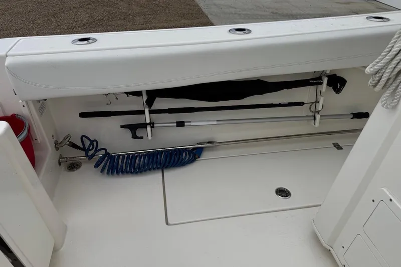 Slide: The Image of 2023 Cobia 301 Center Console boat storage compartment with fishing gear and coiled hose. - 7