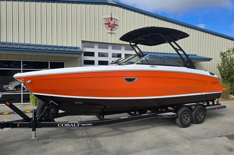 The Image of 2024 Cobalt R8 boat in vibrant orange on a trailer outside a marine facility. - 1