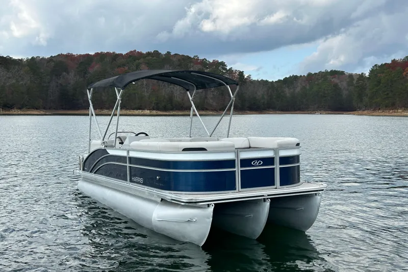 Slide: The Image of 2023 Harris Cruiser 230 pontoon boat on a serene lake with forested shoreline. - 2