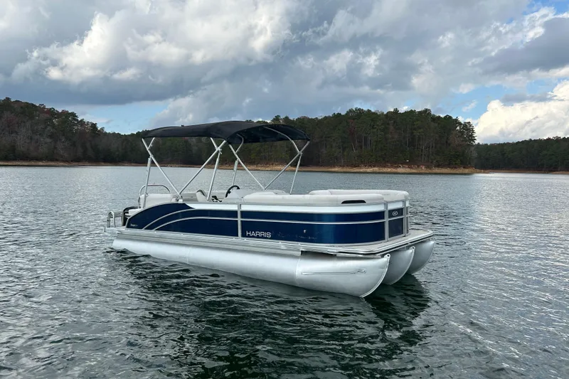 Slide: The Image of 2023 Harris Cruiser 230 pontoon boat on a serene lake with forested shoreline. - 3