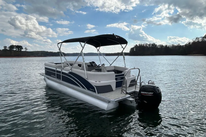 Slide: The Image of 2023 Harris Cruiser 230 pontoon boat on a serene lake under a partly cloudy sky. - 7