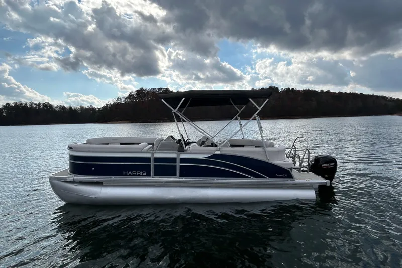 Slide: The Image of 2023 Harris Cruiser 230 pontoon boat on a serene lake under cloudy skies. - 8