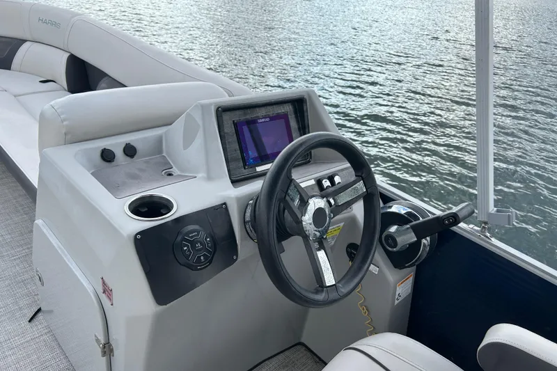 Slide: The Image of 2023 Harris Cruiser 230 boat dashboard with steering wheel and control panel on water. - 9