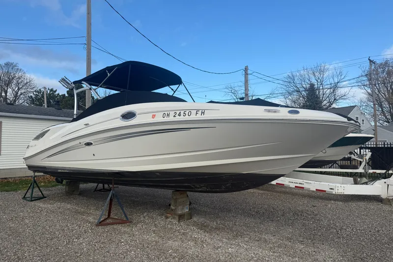 Slide: The Image of 2013 Sea Ray 300 Sundeck boat on stands, with a black canopy, parked outdoors. - 30