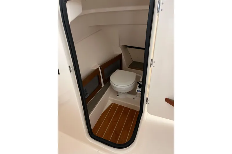Slide: The Image of 2024 Grady-White Freedom 235 boat interior with compact marine toilet and wooden flooring. - 5
