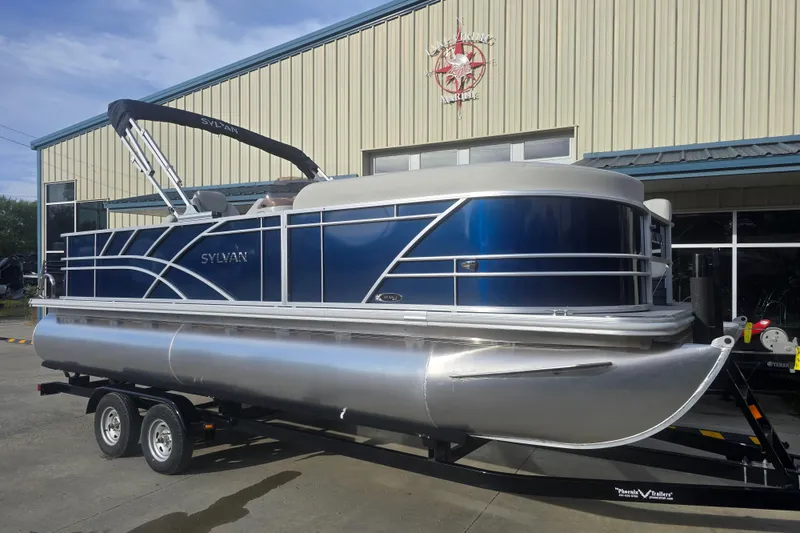 Slide: The Image of 2025 Sylvan Mirage Fish 8522 Party Fish pontoon boat on trailer outside a marine shop. - 9