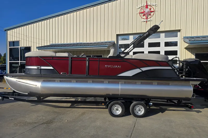 Slide: The Image of 2024 Sylvan L3 LZ pontoon boat on trailer outside a marine dealership. - 2