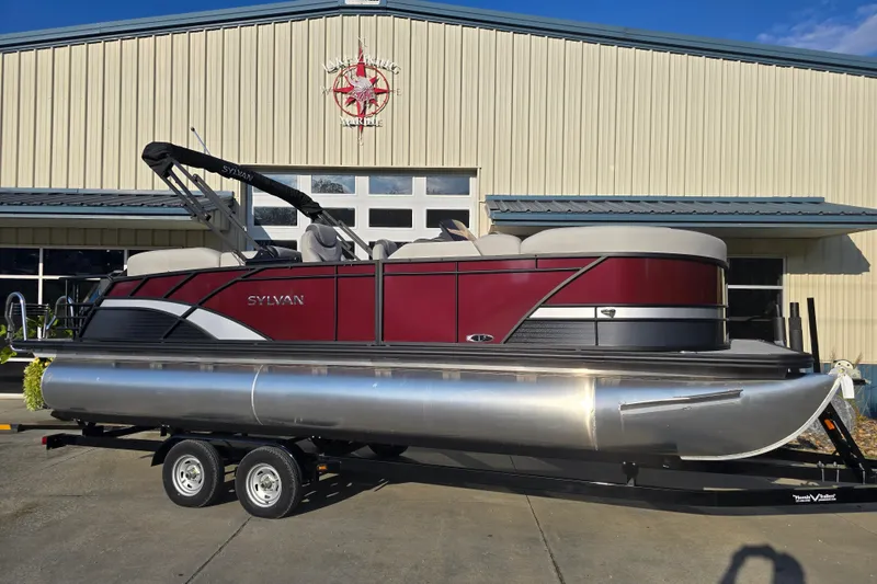 Slide: The Image of 2024 Sylvan L3 LZ pontoon boat on trailer, parked outside a marine building. - 8