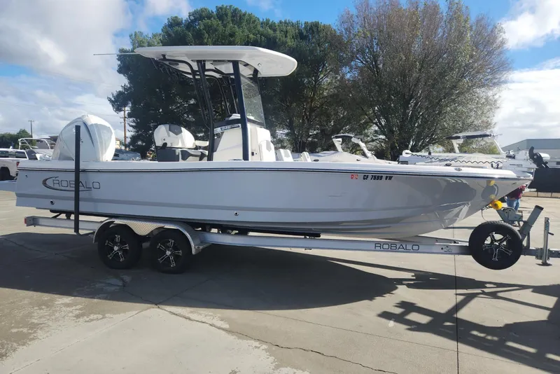 The Image of 2024 Robalo 246 Cayman boat on trailer, parked outdoors under a cloudy sky. - 1