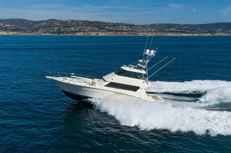 Slide: The Image of 1991 Hatteras 58 Convertible yacht cruising on open water, scenic coastal backdrop. - 2