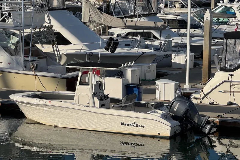 Slide: The Image of 2023 NauticStar 242L Offshore boat interior with seating and cup holders at dock. - 3