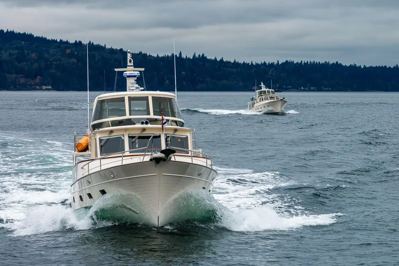 Slide: The Image of 2026 Fleming 55 Pilothouse yachts cruising on a scenic, overcast waterway. - 7