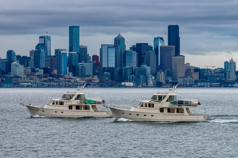 Slide: The Image of Two Fleming 55 Pilothouse yachts cruising near a city skyline under cloudy skies. - 6