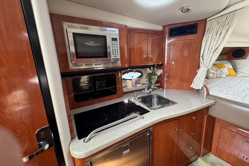 Slide: The Image of 2008 Crownline 340 CR yacht interior with kitchenette, featuring microwave, sink, and cozy sleeping area. - 13