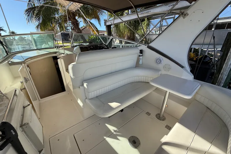 Slide: The Image of 2003 Cruisers Yachts 3075 Express interior with white seating and table, under palm trees. - 9