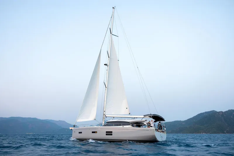 Slide: The Image of 2026 Moody 48 Deck Saloon sailing on open sea with mountainous backdrop. - 9