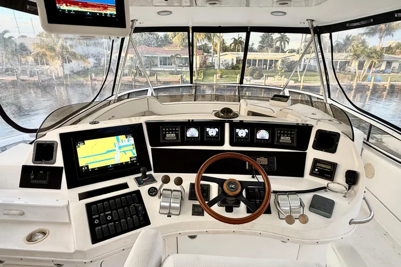 Slide: The Image of 1999 Sea Ray 560 Sedan Bridge helm with navigation screens and controls, overlooking waterfront homes. - 7