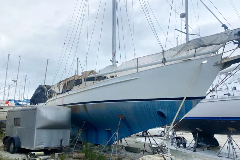 Slide: The Image of 1966 Vanguard Bermudian Sloop sailboat on land, with trailer nearby, under cloudy sky. - 4