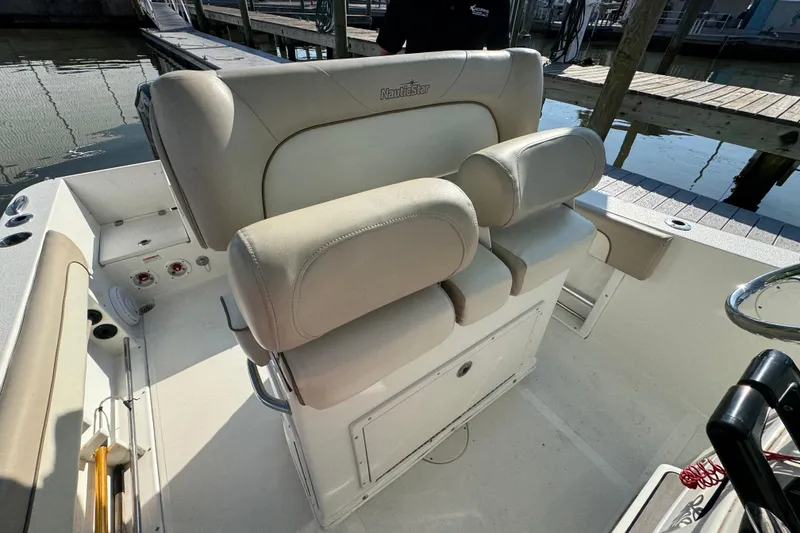 Slide: The Image of 2015 NauticStar 2500XS Offshore boat interior with beige seating at a marina. - 13
