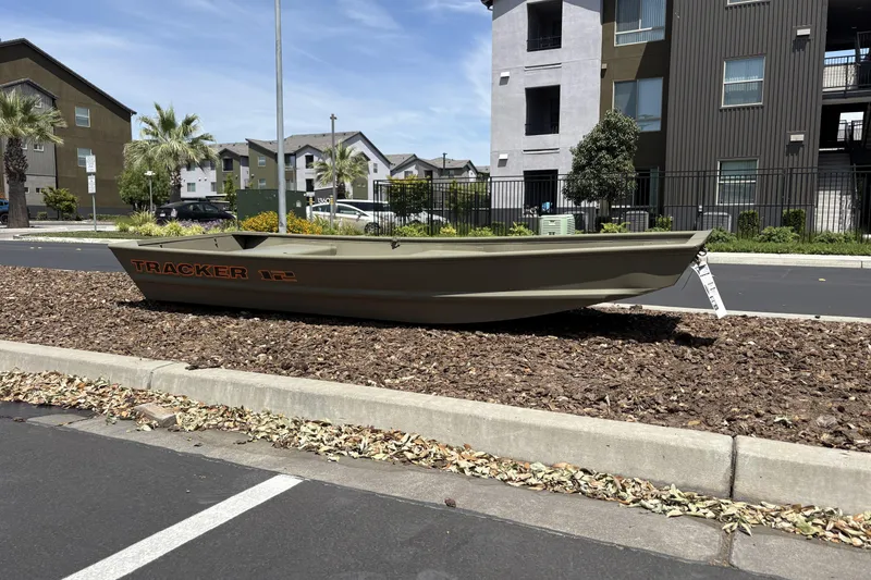Slide: The Image of 2026 Tracker Grizzly 12 Jon boat displayed on landscaped area near residential buildings. - 2
