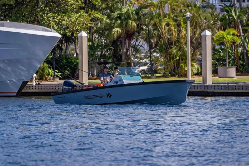 Slide: The Image of 2024 Goldfish 28 Tender boat cruising near a marina with lush greenery. - 30