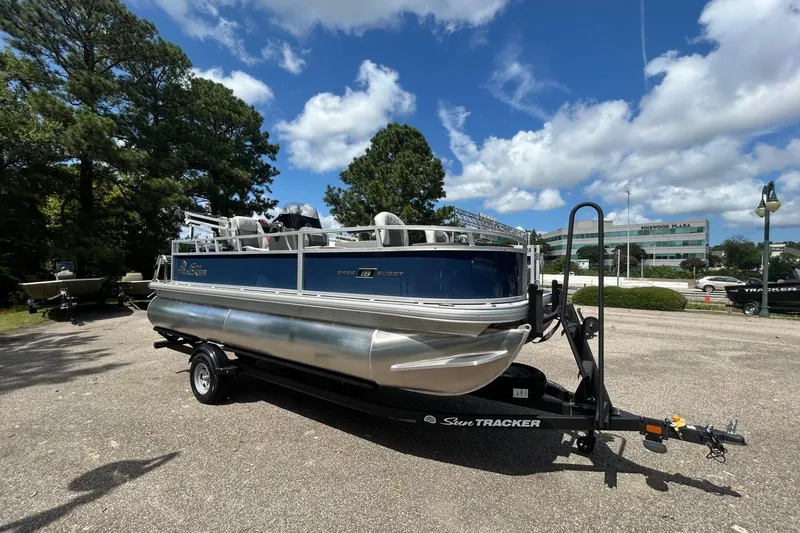 Slide: The Image of 2026 Sun Tracker Bass Buggy 18 DLX pontoon boat on trailer, parked outdoors. - 2